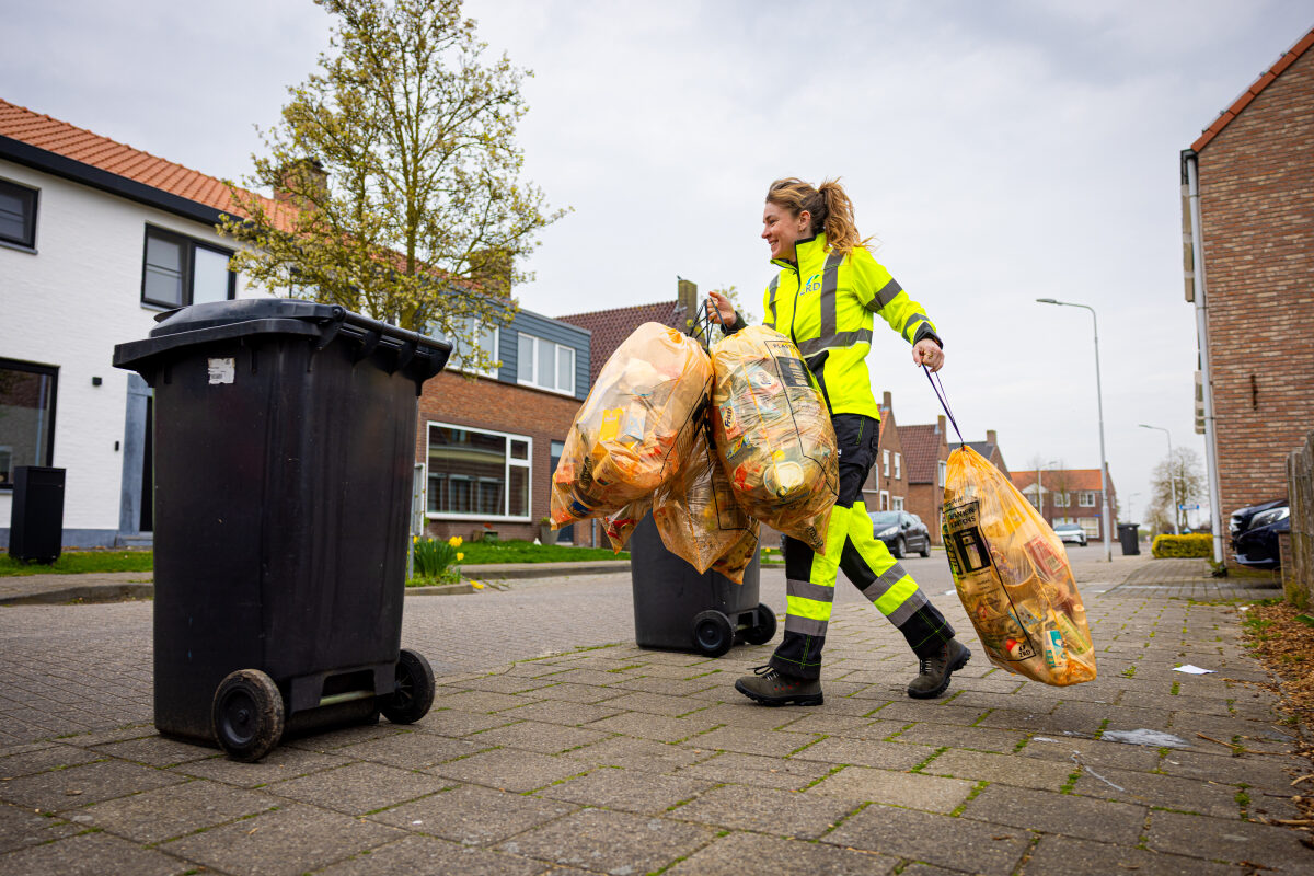 Een medewerkster van een afvalinzamelbedrijf haalt zakken met recyclebaar plastic op bij woningen
