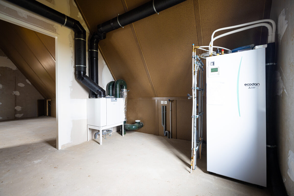 Een ventilatiesysteem (WTW-unit) en een binnenunit van een warmtepomp op een zolder van een nieuwbouwwoning
