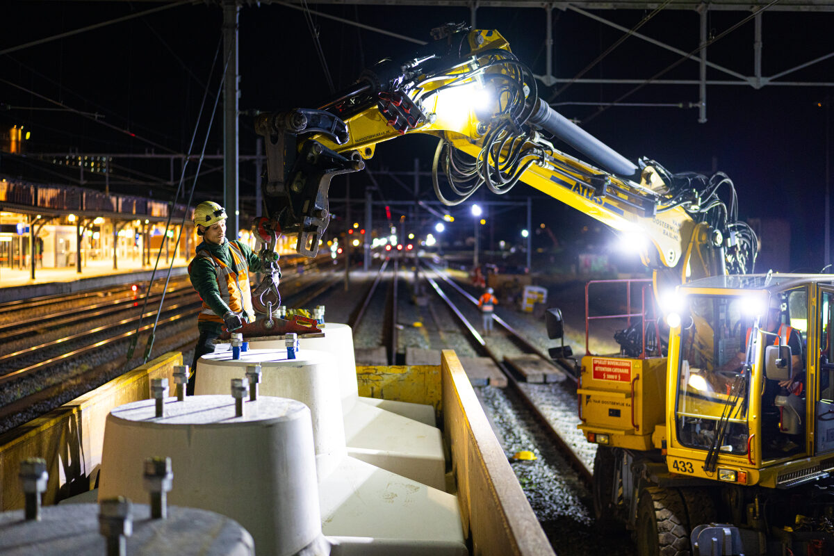 Een medewerker laadt met behulp van een KROL (KRaan Op Lorries) funderingsblokken voor de bovenleiding uit vanaf een trein bij de bouw van een extra perroneiland op station Nijmegen