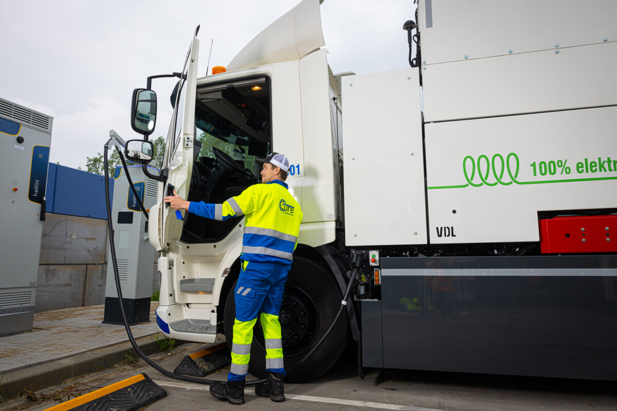 Een medewerker van een afvalinzamelaar bij een elektrische vrachtwagen die aan de lader hangt